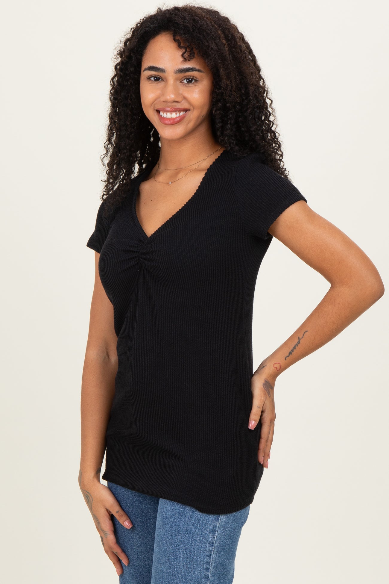 woman wearing a black short sleeve ribbed top with a twist detail at the neckline and paired with denim jeans