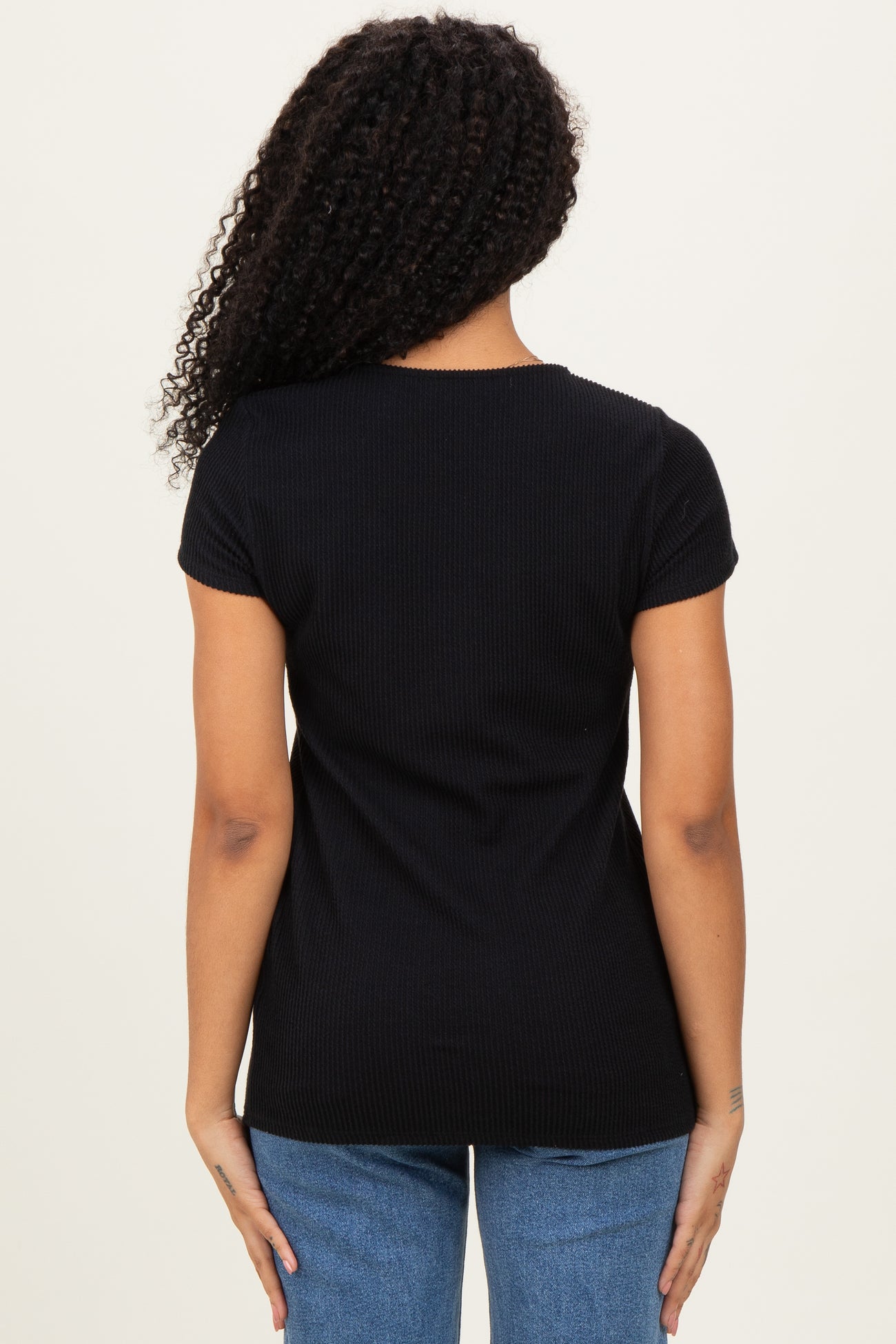 woman wearing a black ribbed short sleeve top, viewed from the back, paired with blue jeans