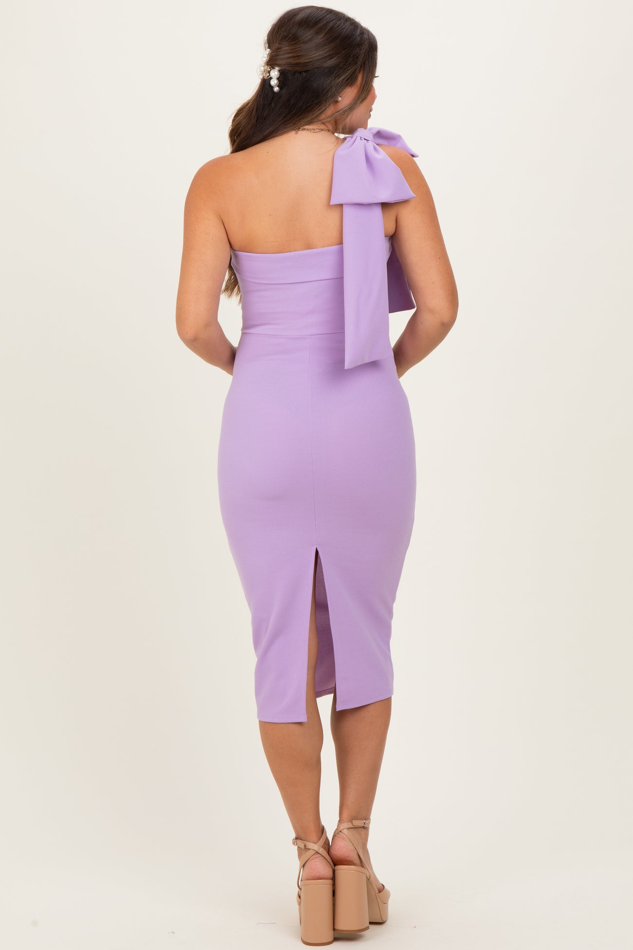 woman wearing a lavender one-shoulder maternity dress with a bow detail and a back slit