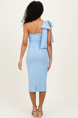 woman wearing a light blue one-shoulder midi dress with a bow detail on the shoulder and a fitted silhouette