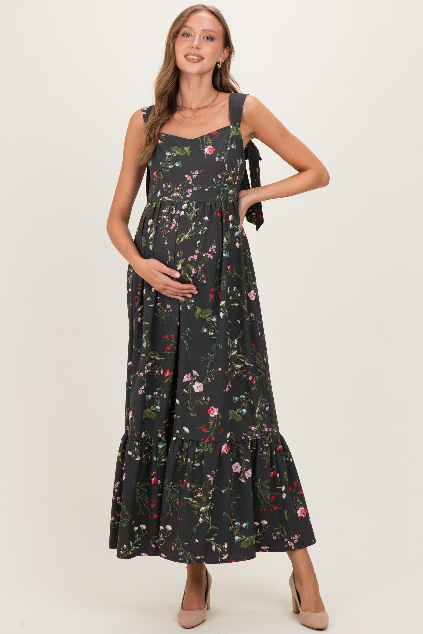 woman wearing a floral print maternity dress with tie straps and a ruffled hem, gently cradling her baby bump