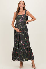 woman wearing a floral print maternity dress with tie straps and a ruffled hem, gently cradling her baby bump