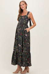 woman wearing a black floral print maternity maxi dress with pockets and ruffle hem, showcasing her baby bump