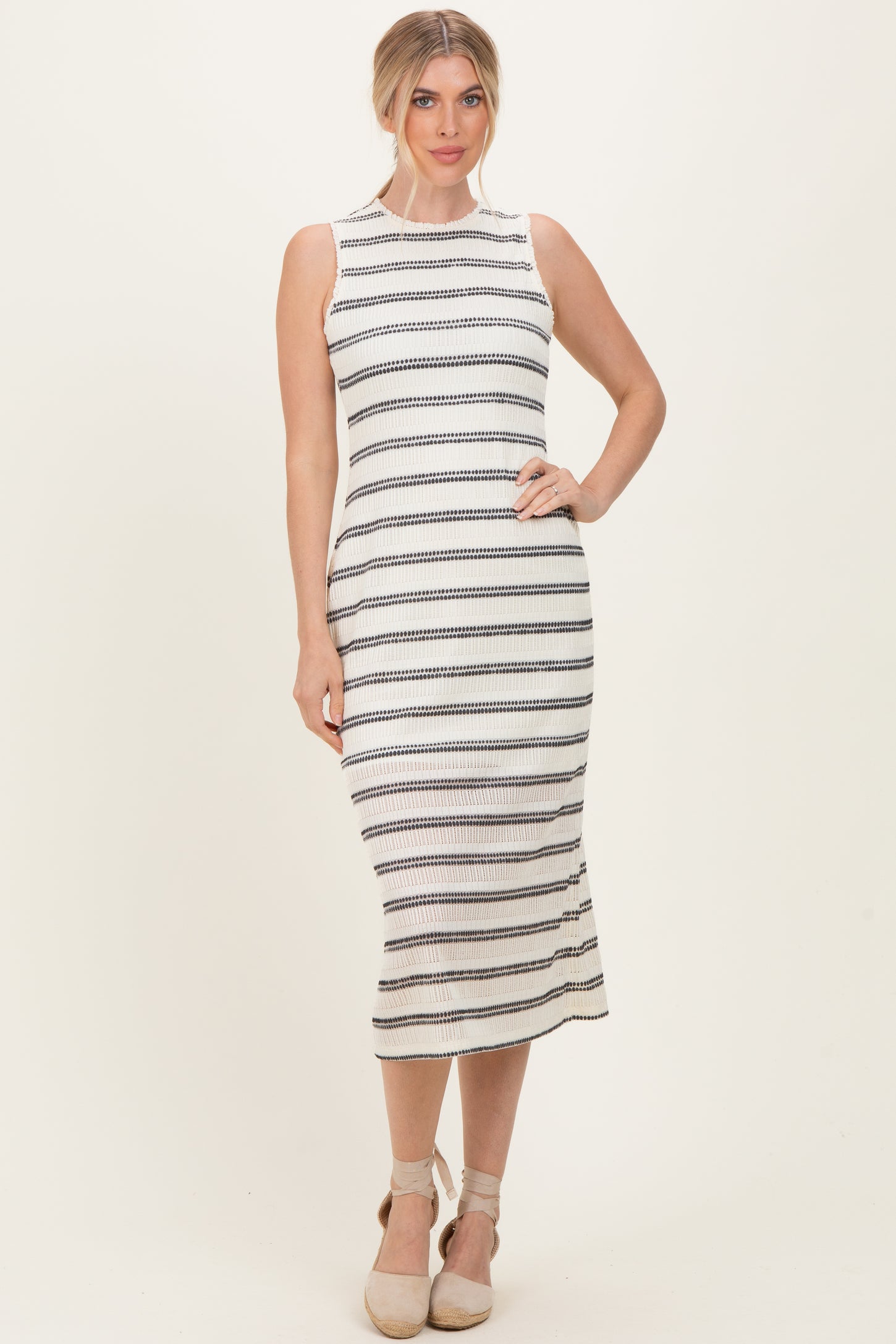 woman wearing a sleeveless white and black striped midi dress with a fitted silhouette and a round neckline