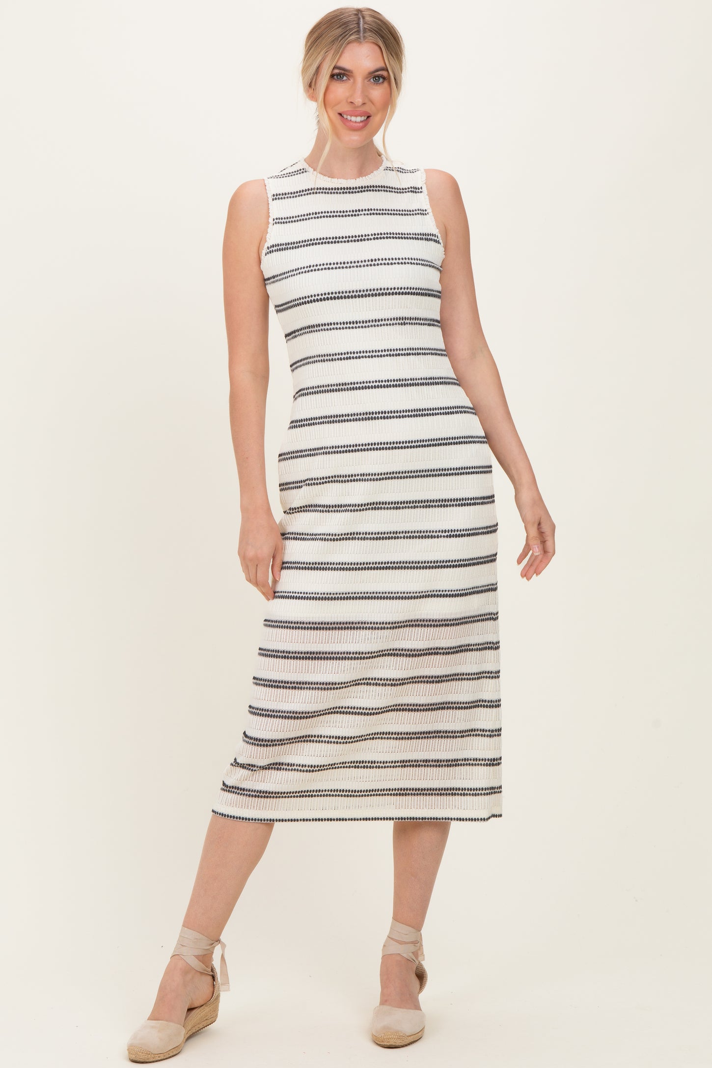 woman wearing a white and navy striped sleeveless midi dress with a fitted silhouette and espadrille wedges