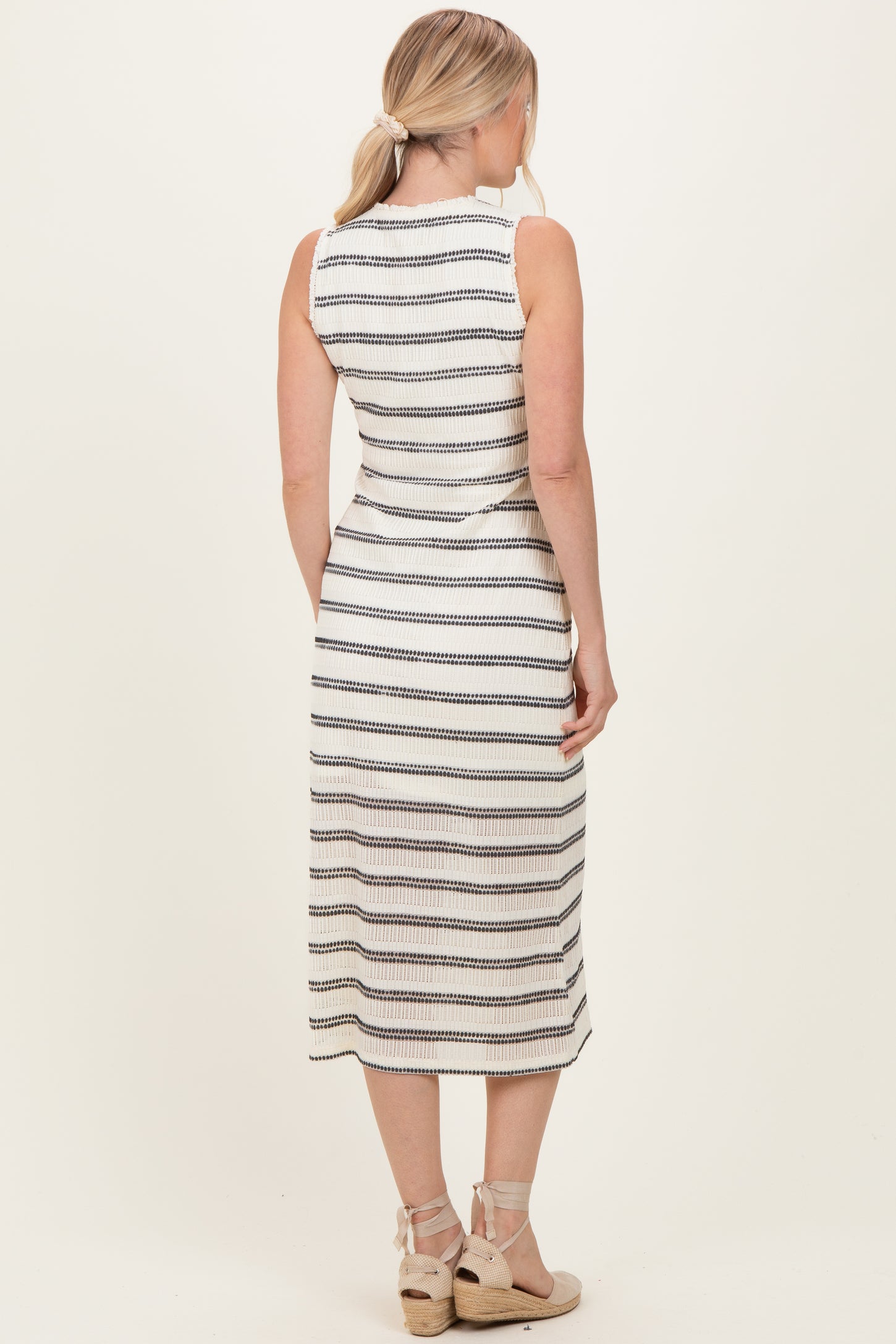 woman wearing a sleeveless white and black striped midi dress with a fitted silhouette and a back view