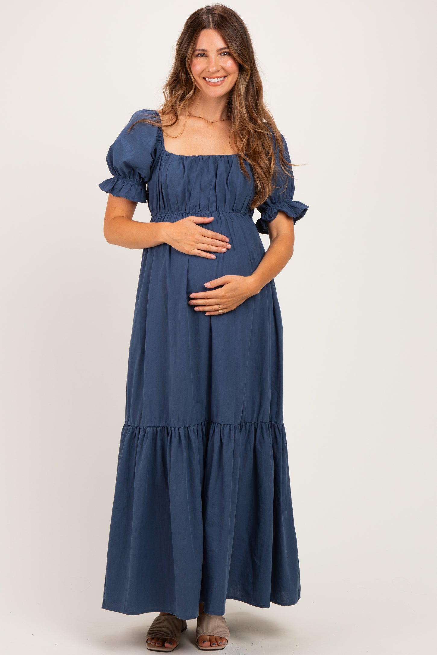 woman wearing a navy blue maternity maxi dress with puff sleeves and a gathered bodice, holding her baby bump
