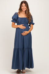 woman wearing a navy blue maternity maxi dress with puff sleeves and a gathered bodice, holding her baby bump