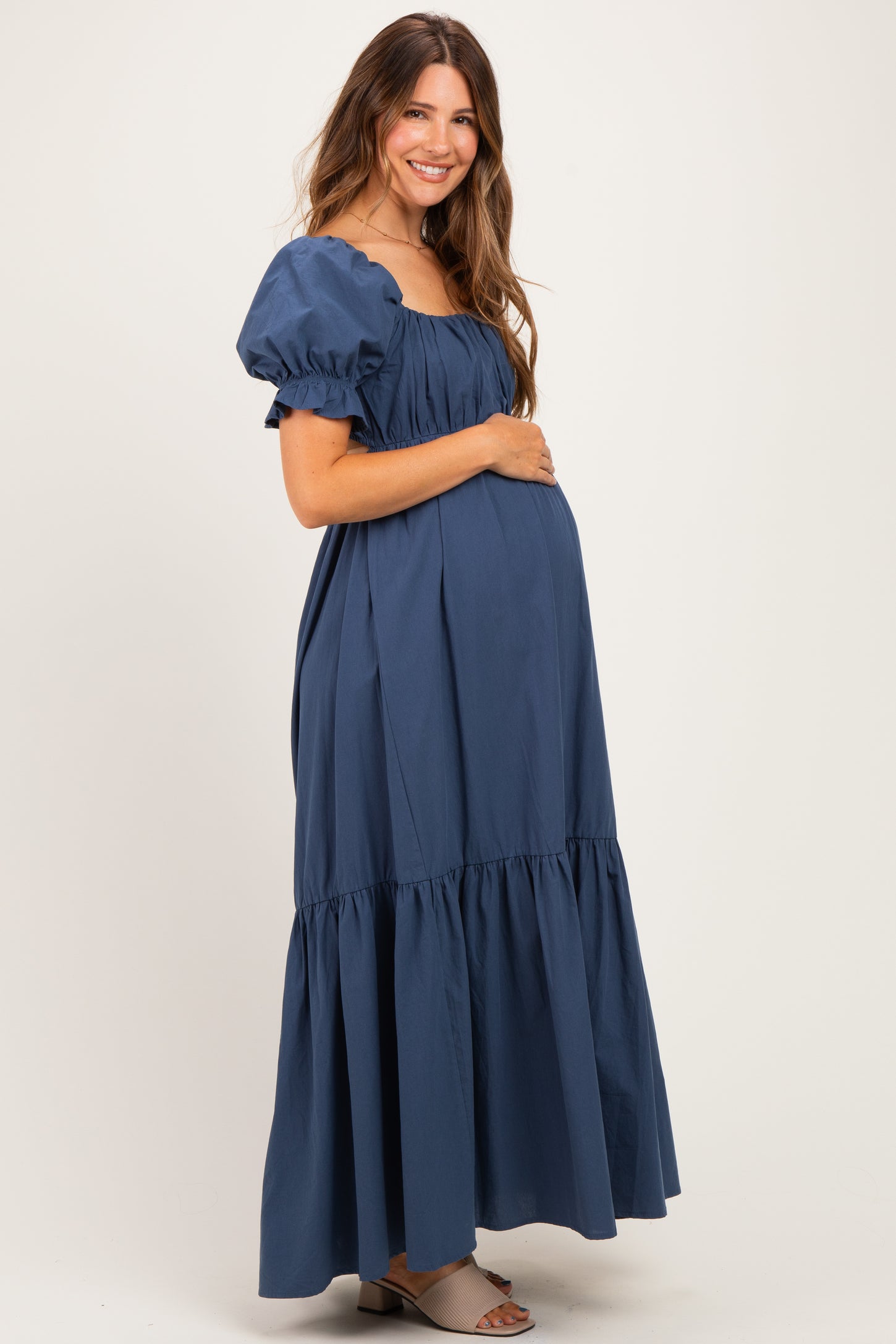 woman wearing a navy blue maternity maxi dress with puff sleeves and a tiered skirt, showcasing her baby bump