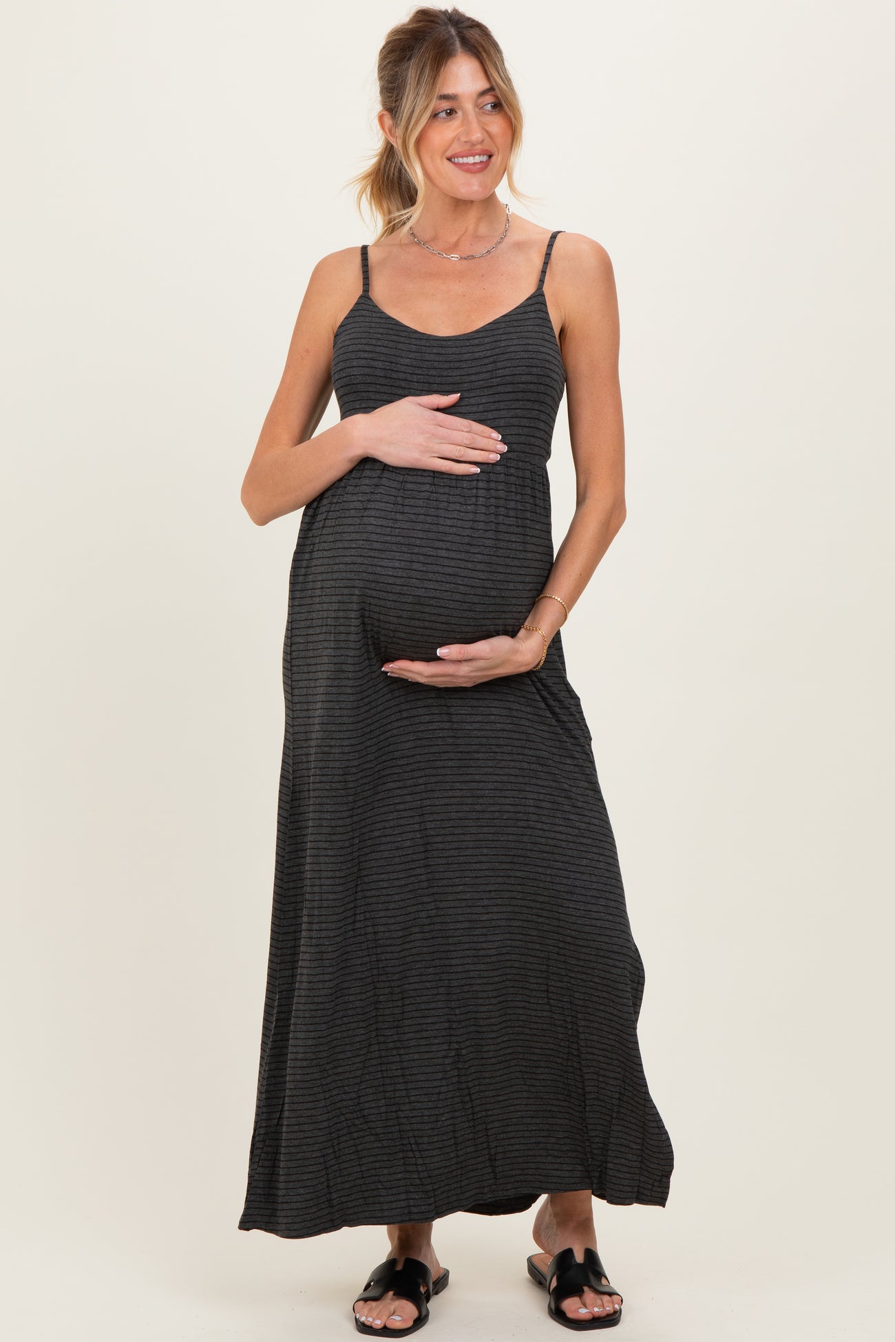 woman wearing a black striped maternity maxi dress and holding her baby bump