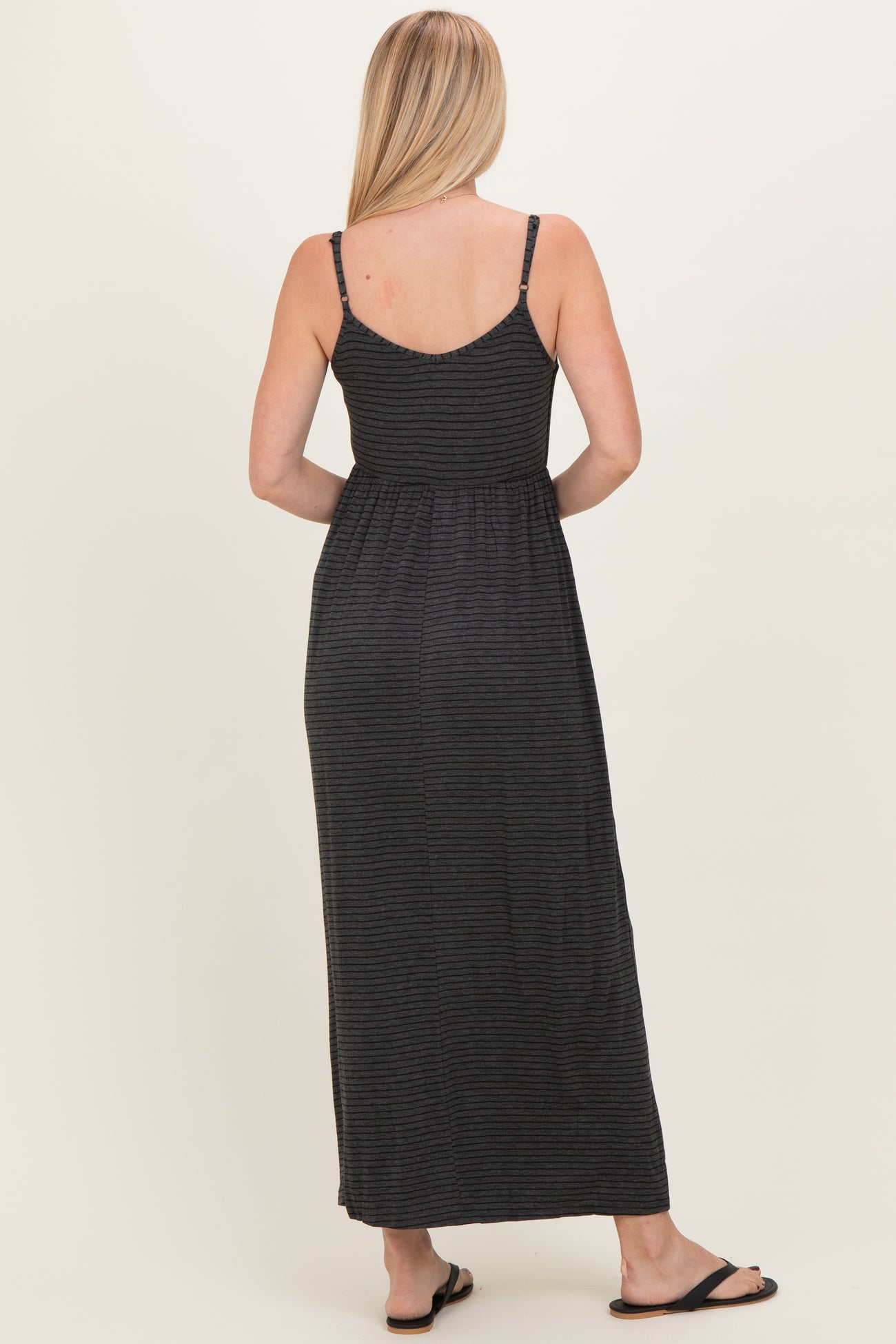 woman wearing a black and gray striped maxi dress with adjustable straps and a cinched waist