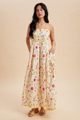 woman wearing a yellow floral maxi dress with pockets and spaghetti straps, standing against a neutral background