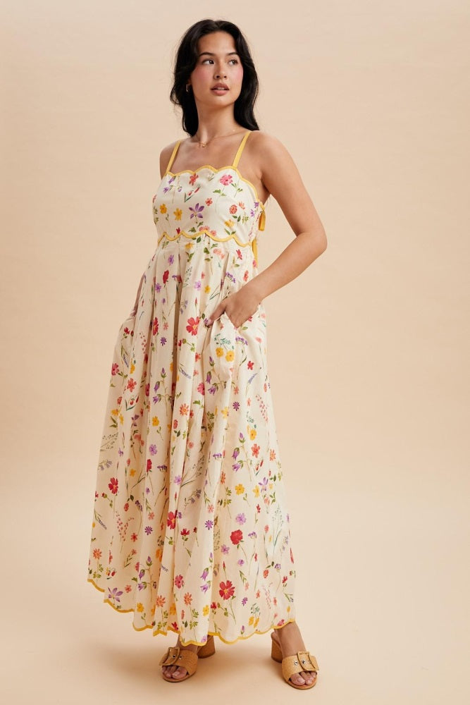 woman wearing a floral printed cream maxi dress with spaghetti straps and pockets, styled with yellow trim