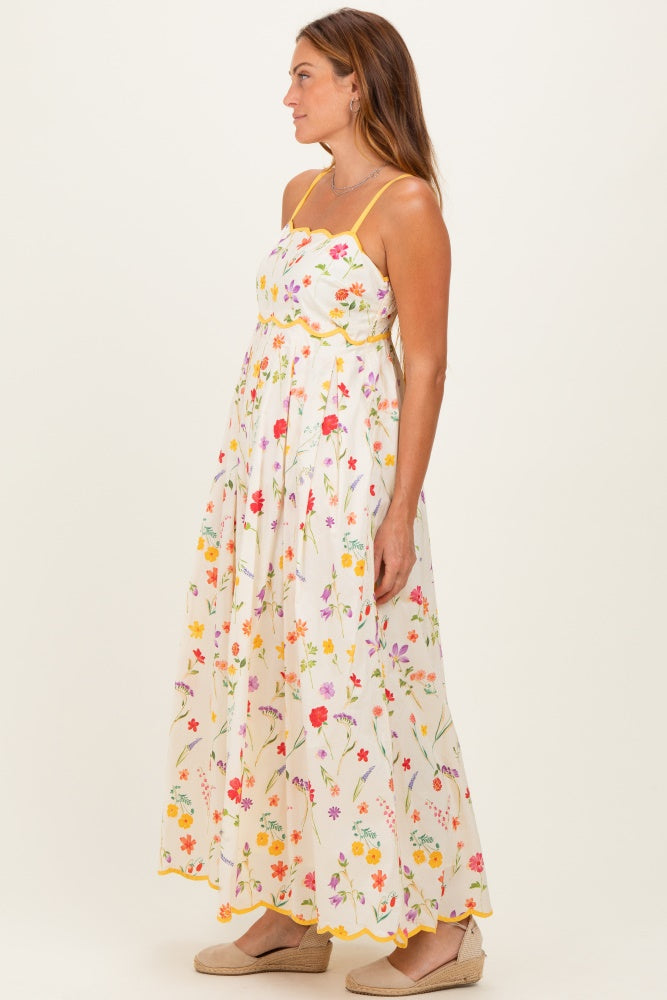 woman wearing a sleeveless floral maxi dress in white with colorful designs and yellow trim