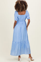 woman wearing a blue polka dot maternity maxi dress with puff sleeves and a tiered skirt, showing her baby bump from the back