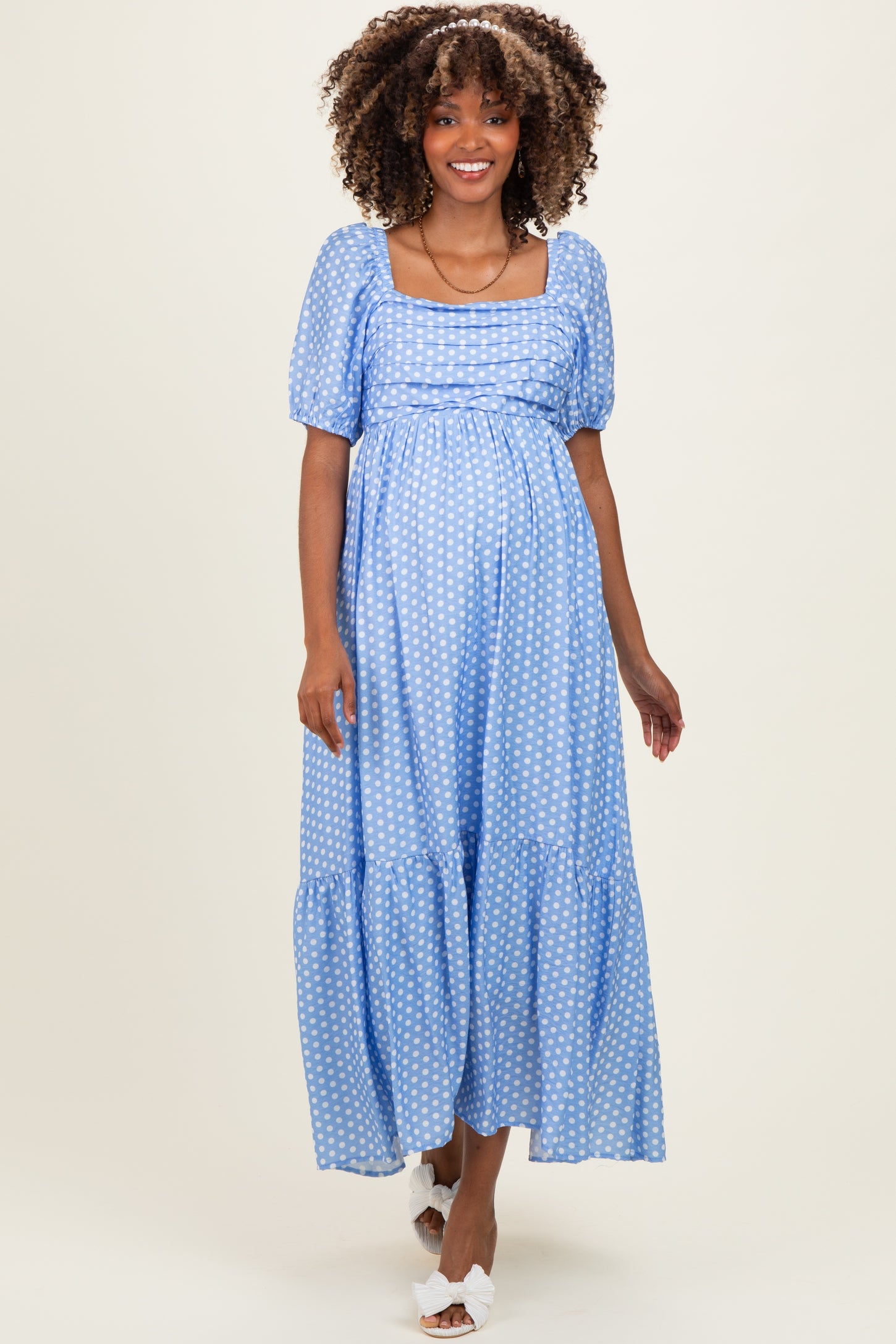 woman wearing a light blue polka dot maternity dress with puff sleeves and a tiered skirt, highlighting her baby bump