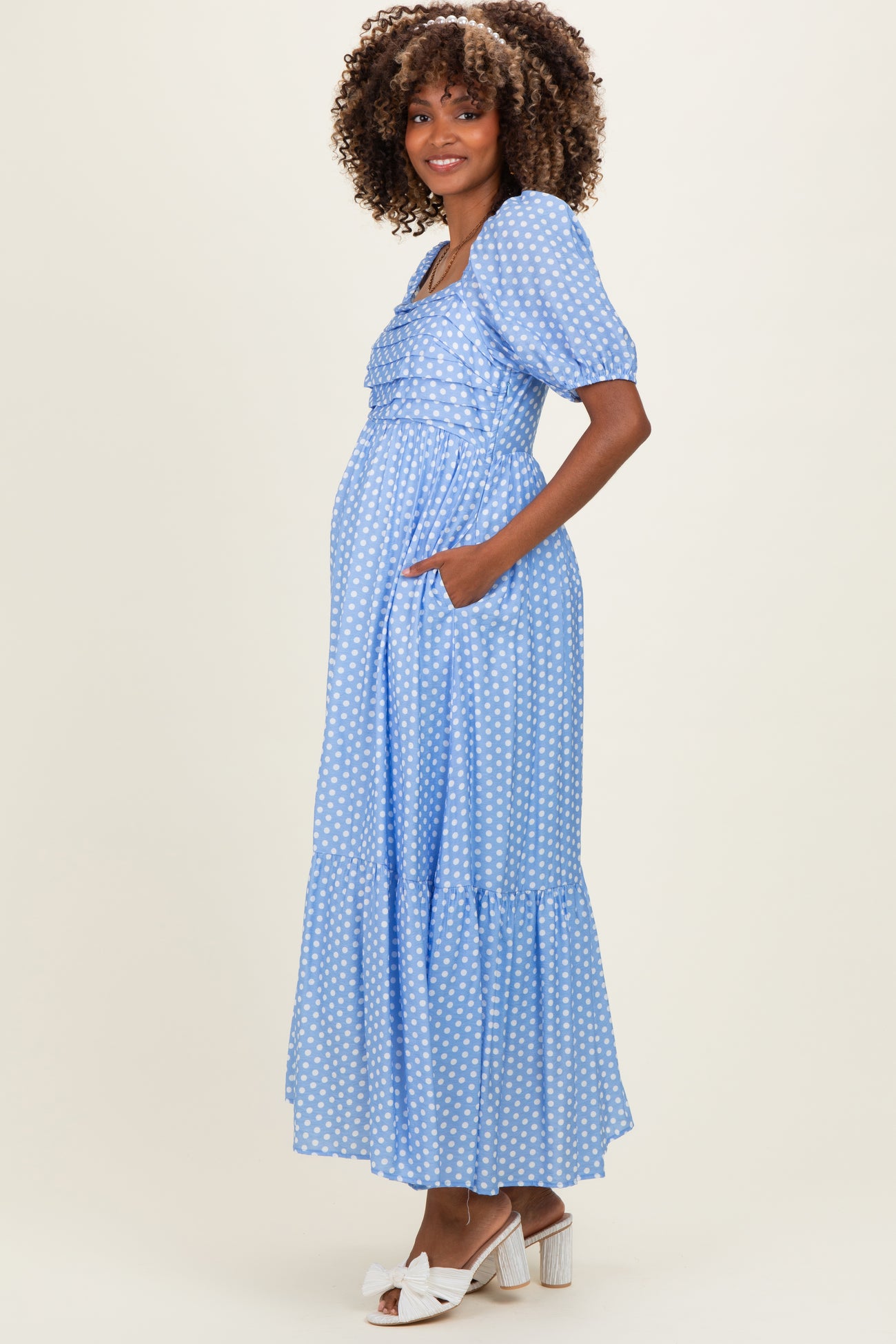 woman wearing a light blue polka dot maternity maxi dress with puff sleeves and pockets, showing her baby bump