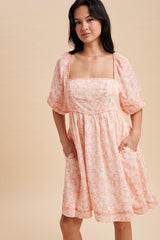 woman wearing a light pink floral square neckline dress with short puff sleeves and pockets
