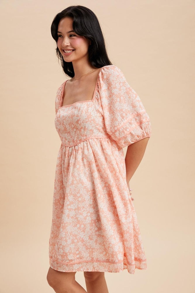 woman wearing a light peach floral print puff sleeve dress with a square neckline and gathered waist