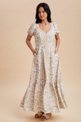 woman wearing a cream floral maxi dress with puff sleeves and pockets, standing on a beige background