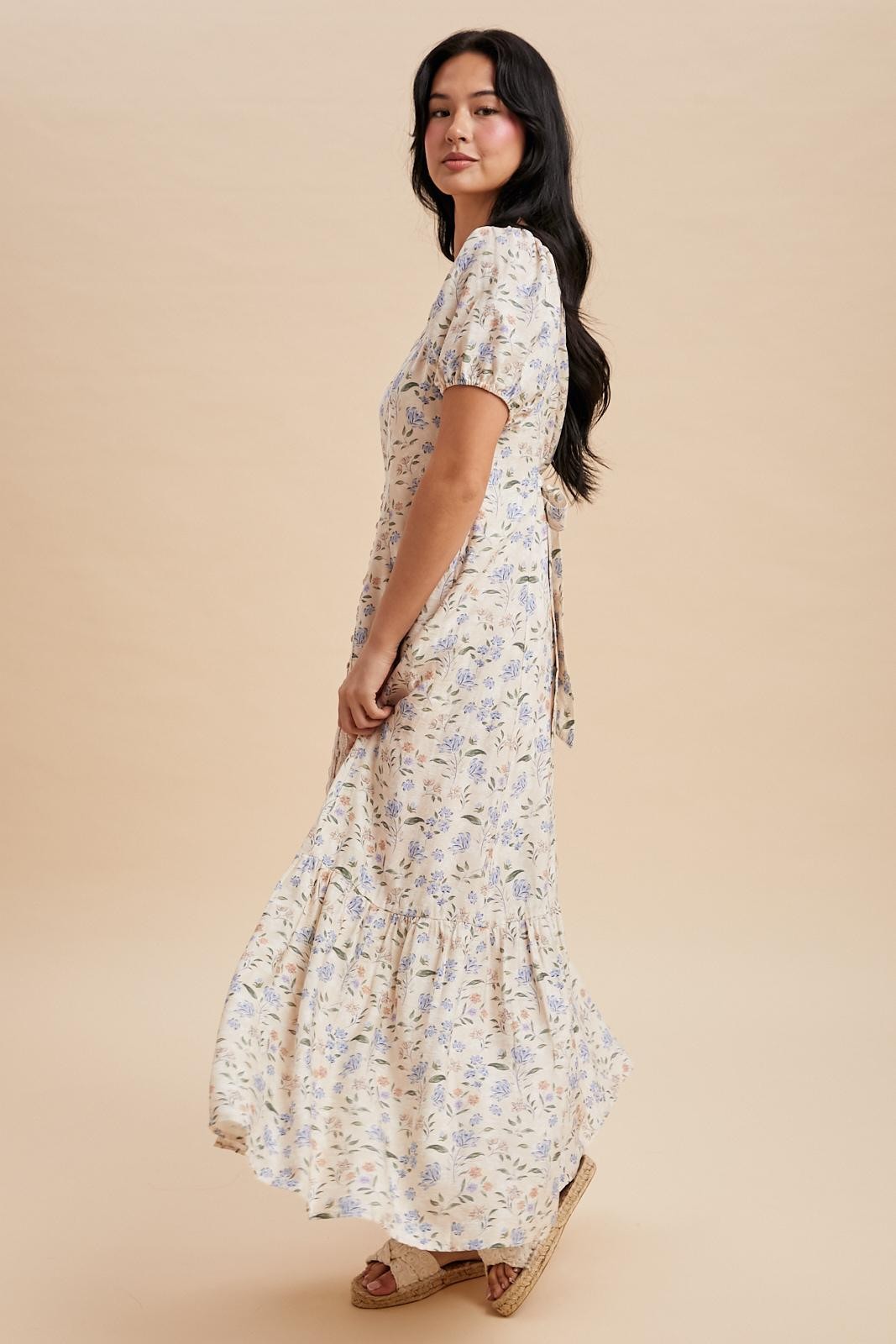 woman wearing a floral maxi dress with puff sleeves and a tied back detail, posed against a neutral background