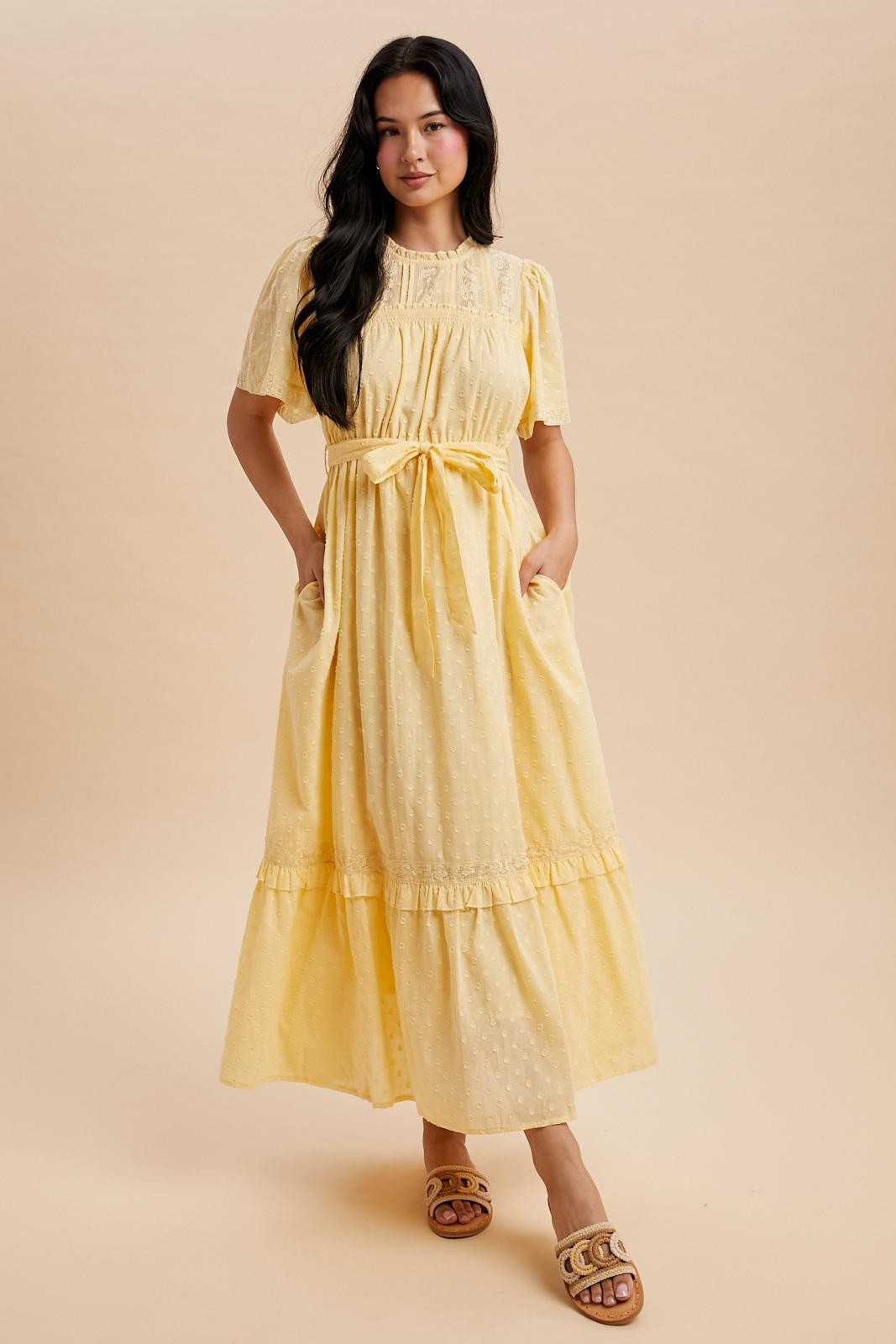 woman wearing a yellow short sleeve maxi dress with a tie waist and pockets, standing against a neutral background