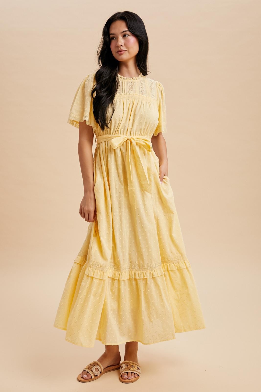 woman wearing a light yellow short sleeve maxi dress with a tie waist and ruffle trim