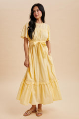 woman wearing a light yellow short sleeve maxi dress with a tie waist and ruffle trim
