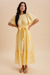 woman wearing a light yellow maxi dress with puff sleeves, a cinched waist, and a tiered hem