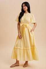 woman wearing a yellow maxi dress with short sleeves, a tie waist, and tiered ruffle hem
