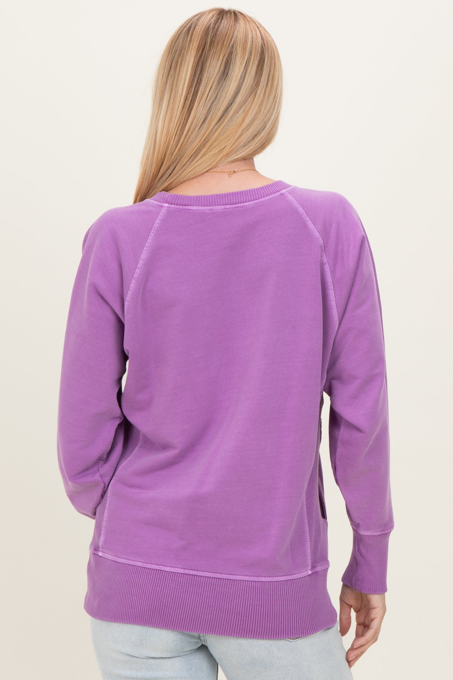 woman wearing a purple long sleeve sweatshirt with a relaxed fit and ribbed hem, shown from the back