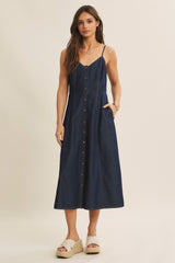 woman wearing a navy blue denim button-up midi dress with thin straps and side pockets