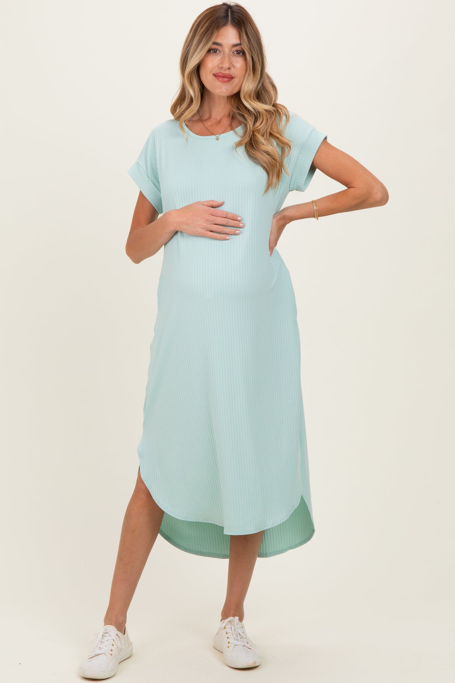 woman wearing a mint green ribbed maternity dress with a curved hem and holding her baby bump