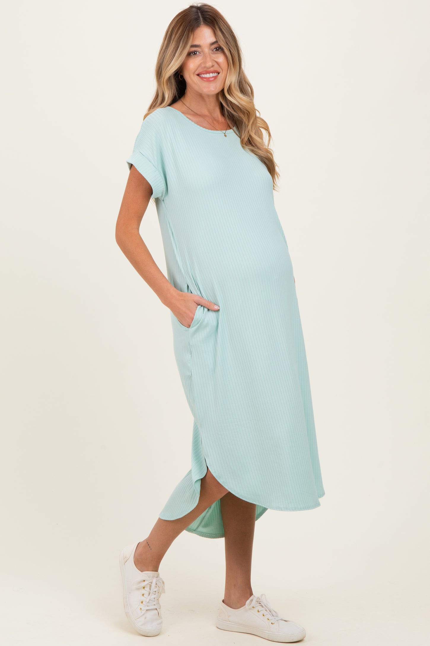 woman wearing a light turquoise maternity dress with short sleeves and pockets, showing her baby bump
