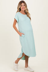 woman wearing a light turquoise maternity dress with short sleeves and pockets, showing her baby bump