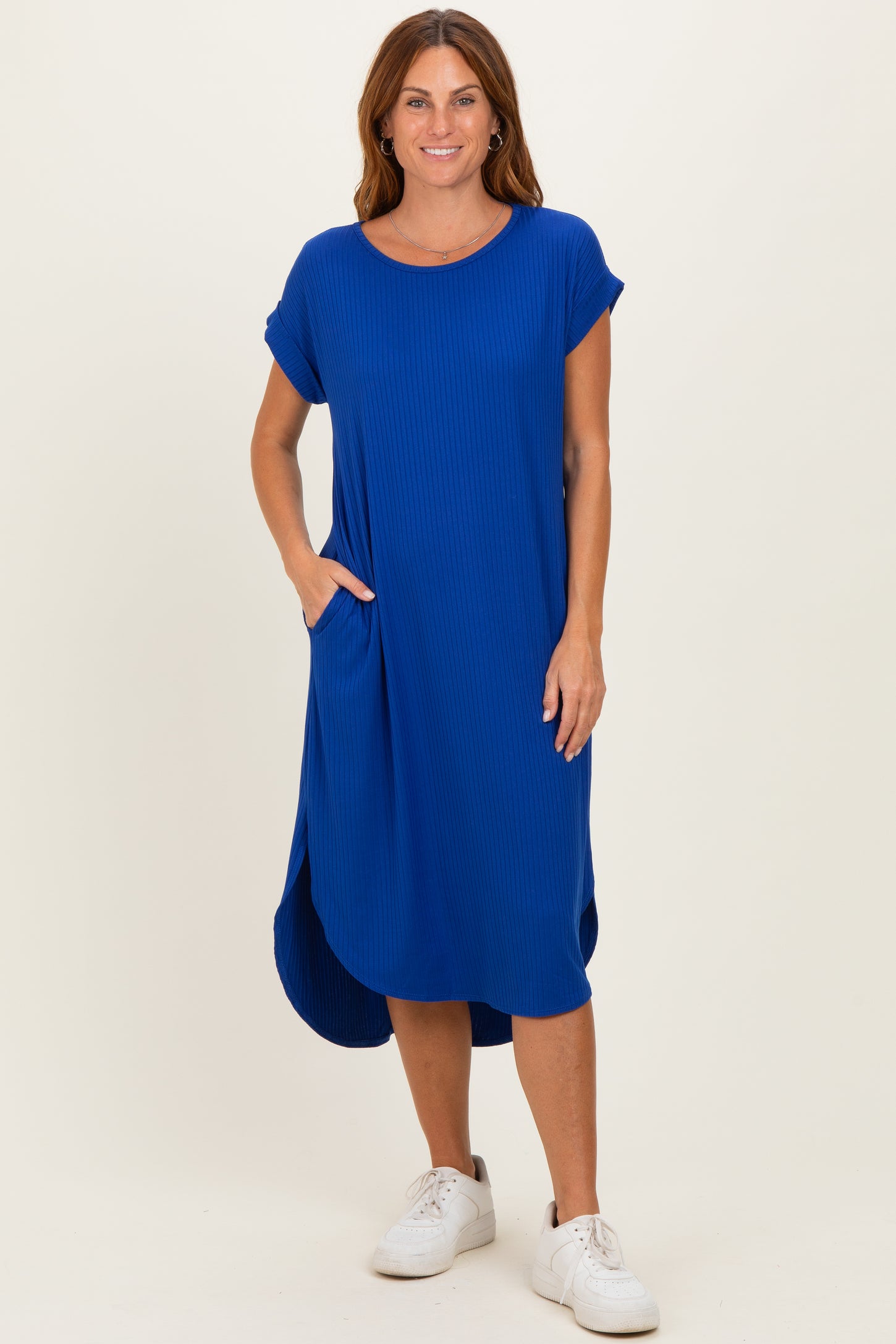 woman wearing a blue ribbed short sleeve midi dress with side pockets and a curved hemline