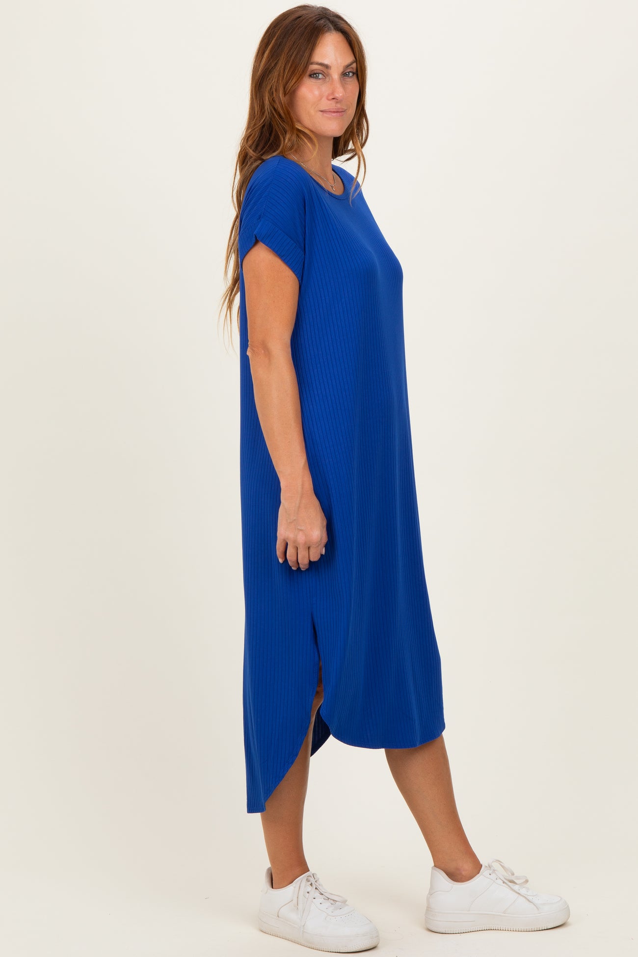 woman wearing a bright blue ribbed midi dress with short sleeves and side slits, styled with white sneakers