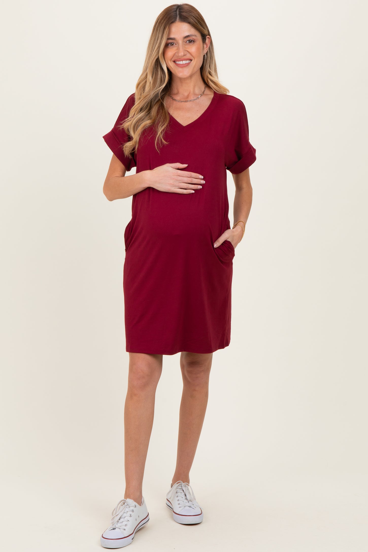 woman wearing a burgundy short sleeve maternity dress with pockets and a visible baby bump