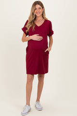 woman wearing a burgundy short sleeve maternity dress with pockets and a visible baby bump