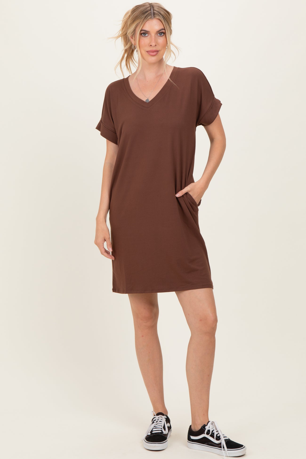 woman wearing a brown short sleeve v-neck dress with pockets and black sneakers