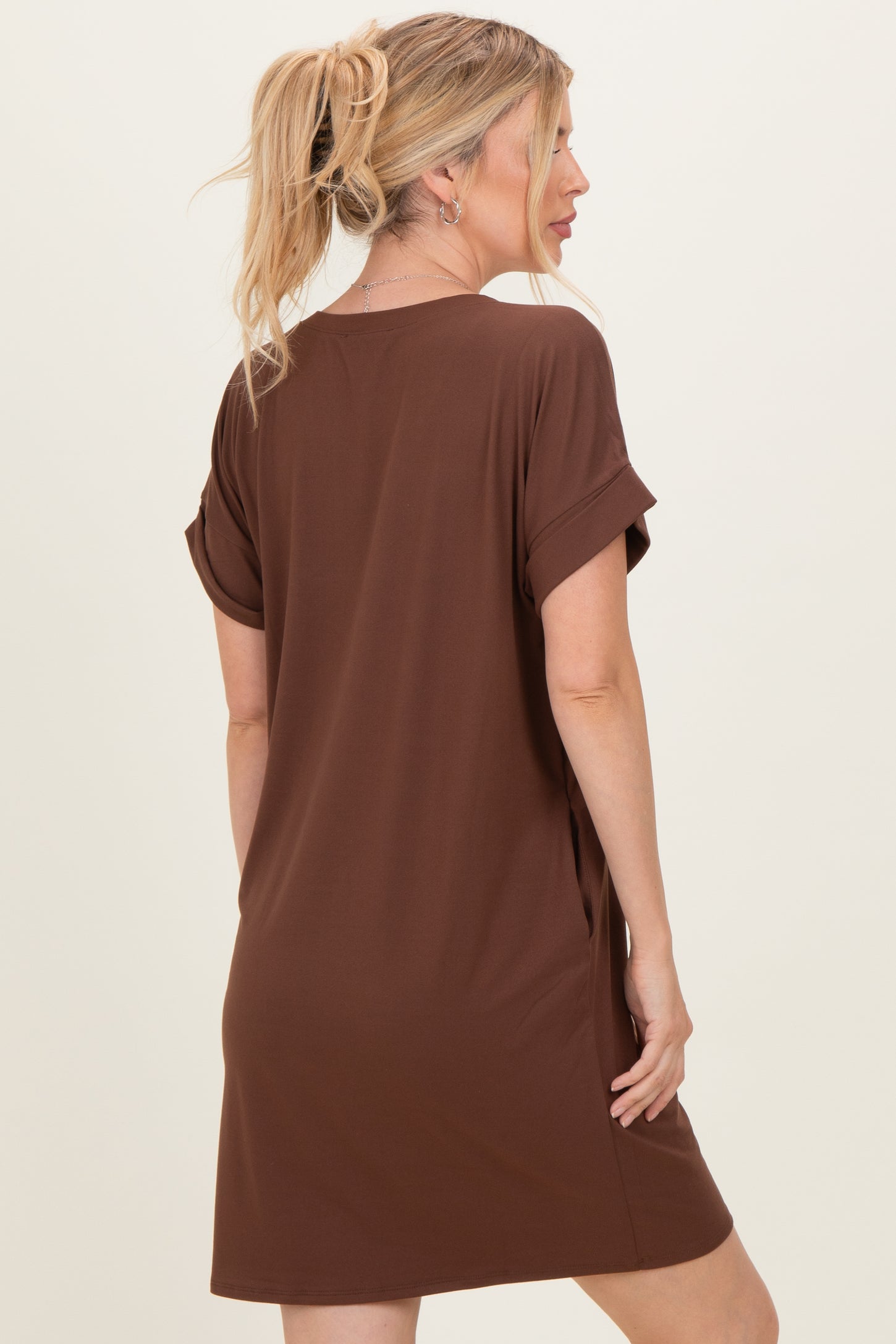 woman wearing a brown short sleeve t-shirt dress with rolled cuffs, standing with her back to the camera