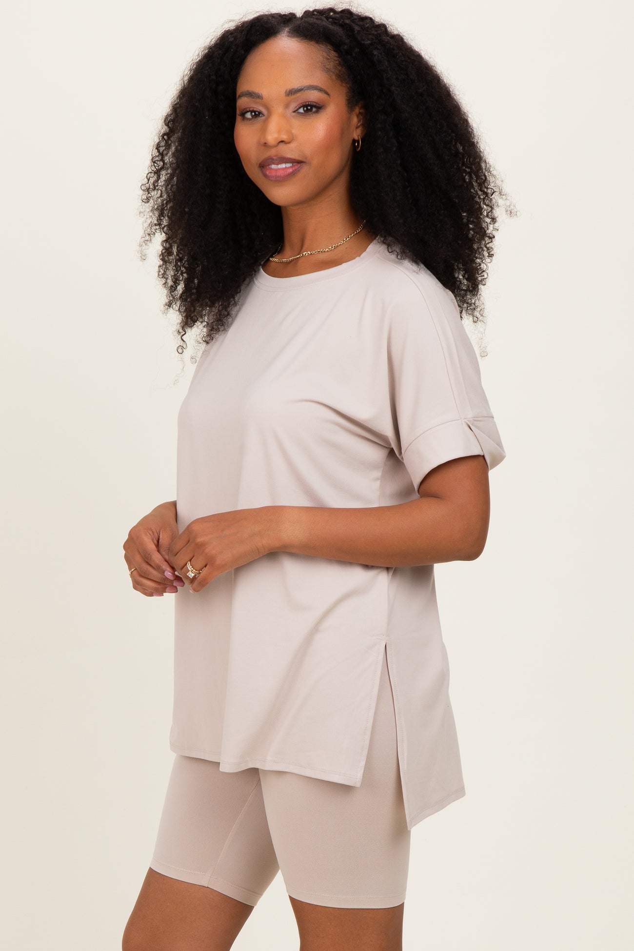 woman wearing a beige oversized t-shirt with rolled sleeves and side slits, paired with beige bike shorts