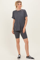 woman wearing a dark gray short sleeve athletic top and matching bike shorts, standing with one hand on her hip