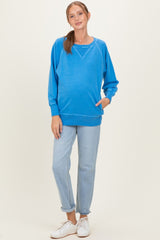 woman wearing a vibrant blue maternity sweatshirt with a relaxed fit and front pocket, paired with light wash jeans and white sneakers