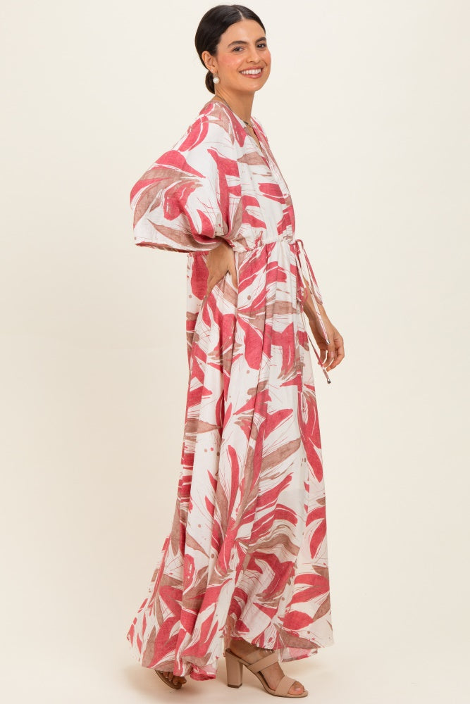 woman wearing a long white maxi dress with pink and brown abstract patterns and a tie waist detail