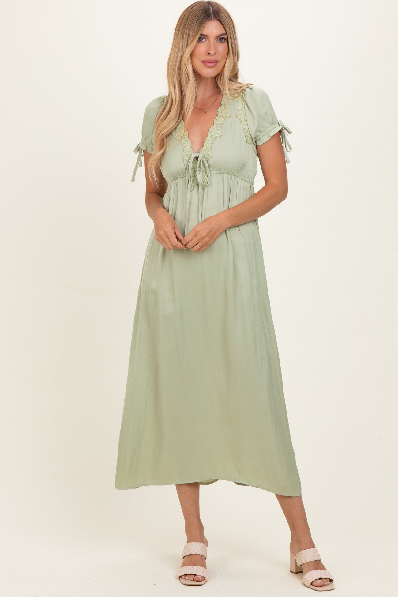 woman wearing a light green maxi dress with short sleeves and lace detailing, posing with hands placed on her waist
