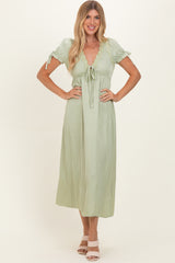 woman wearing a light green midi dress with short sleeves, lace detailing, and a tie waist
