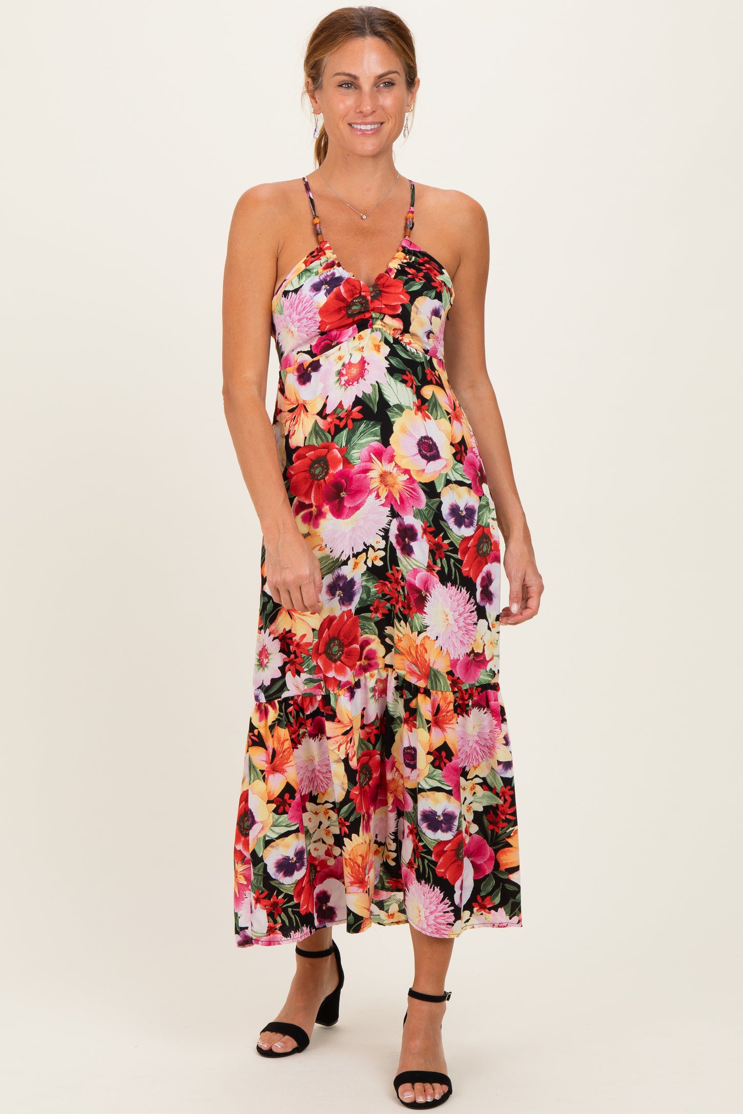 woman wearing a floral maxi dress with a halter neckline and strappy back, standing in heels against a neutral background