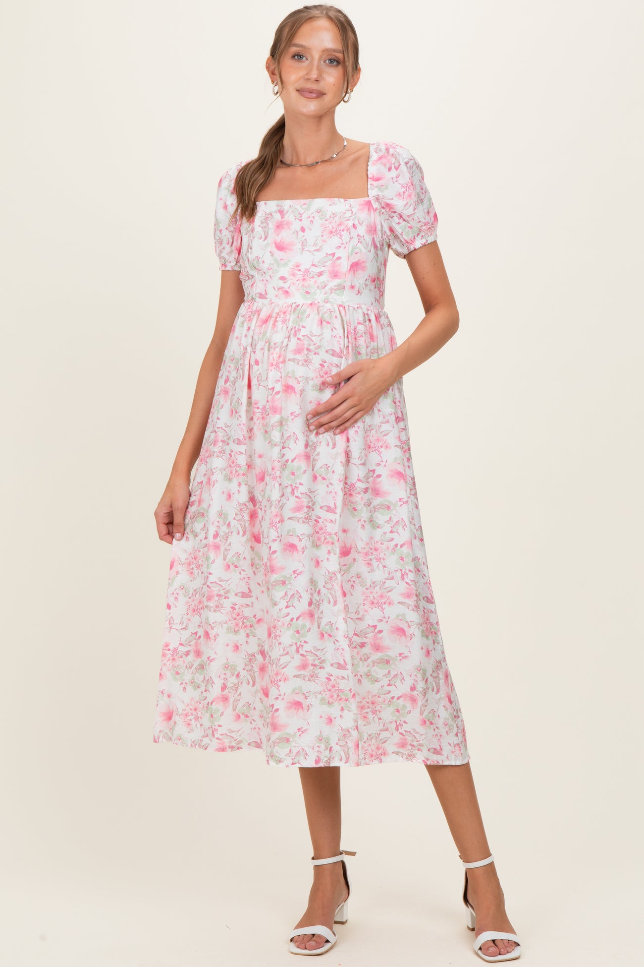 woman wearing a pink floral maternity dress with puff sleeves and a square neckline, holding her baby bump