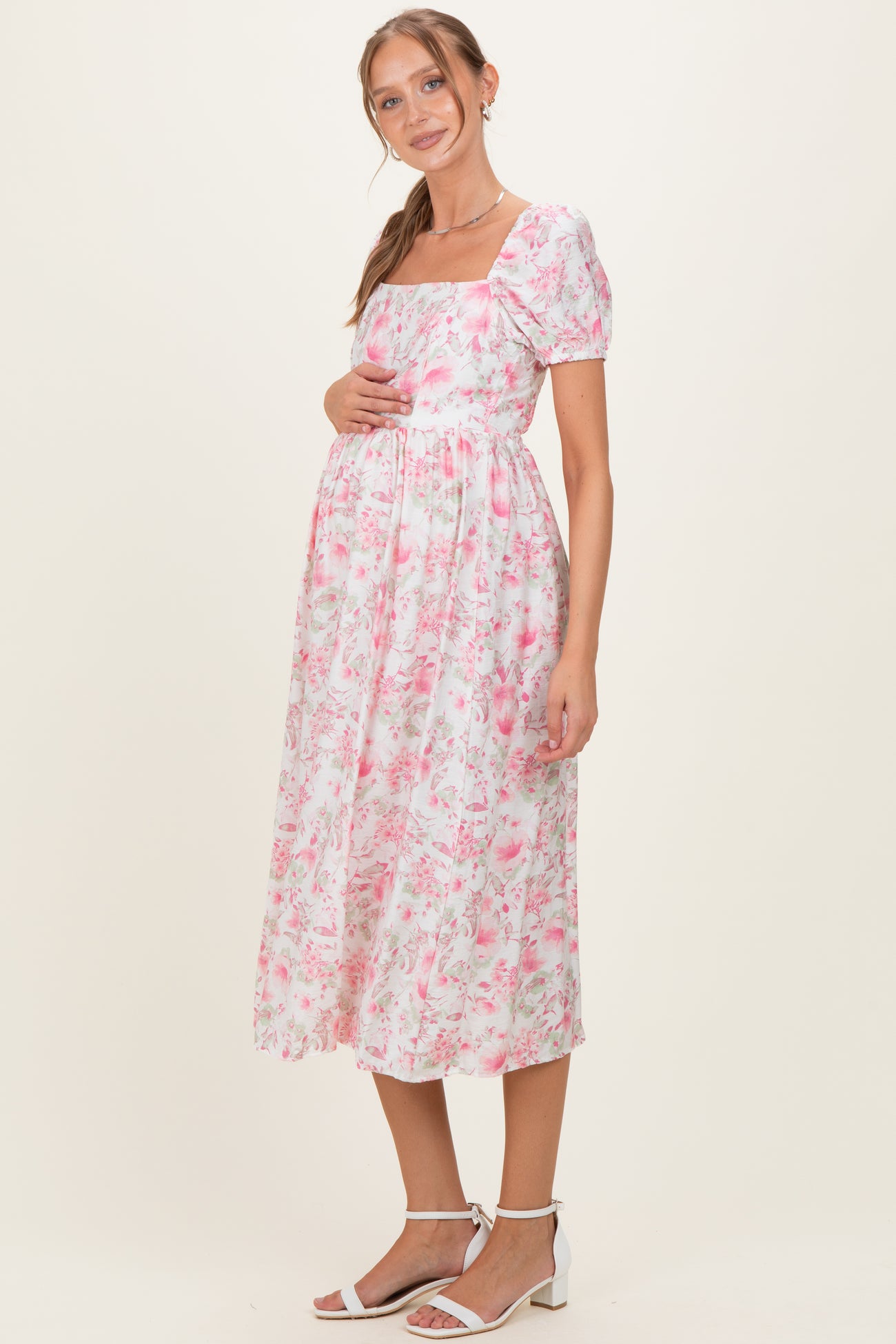 woman wearing a pink floral maternity dress with puff sleeves and holding her baby bump